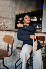 Obraz na płótnie Canvas Charming african american woman model in black jacket and waist bag relaxing in cafe during free time.