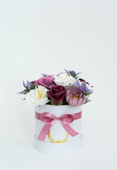 Flowers in bloom: multi-colored red and pink buds in a white round box on a white background.