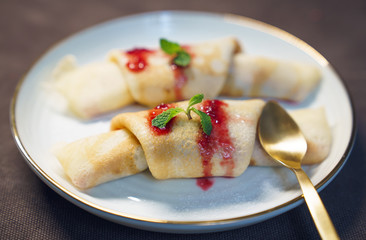 delicious crepes desert with red strawberry sauce, honey and green on white plate served with spoon
