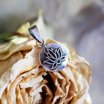 Silver pendant with lotus blossom shape in madala round metal disc, dry rose background