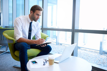 Business entrepreneur making notes while using laptop in modern office