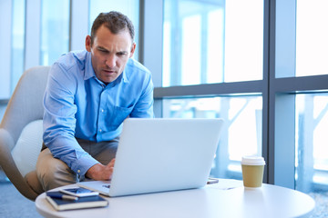 Mature businessman looking seriously at his laptop in modern office