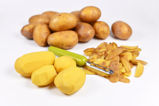 Food preperation with peeled potatos, peels and whole potatoes in background
