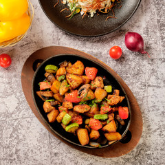 Delicious oven-baked potatoes with herbs and vegetables in a pan, rustic style. Potatoes fried, red cherry tomato, zucchini, onion on gray stone background.