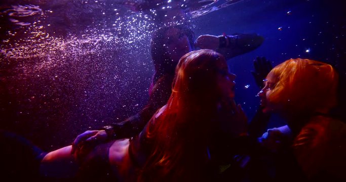 Three Fateful Sexy Girls With Long Hair Are In The Studio Under Water On A Blue Background. They Are Lesbians Hugging And Kissing. Their Hair Is Flying. They Wear Short Tops And Shorts.