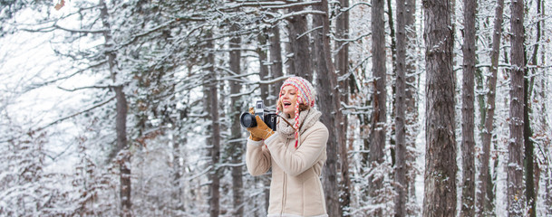 stylish hipster traveler. woman holding photo camera. taking picture in winter forest. Photographer photographing on snowy winter day. happy woman warm clothes fashion. winter travel vacation