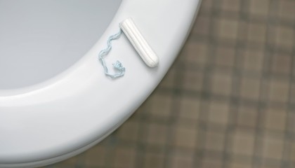 Tampon lies on the toilet bowl. High angle view with soft focus.	