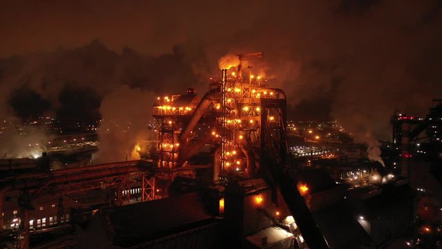 Top view of metallurgical plant blast furnace at night with smokestacks and fire blazing out of the pipe. Industrial panoramic landmark with blast furnance of metallurgical production