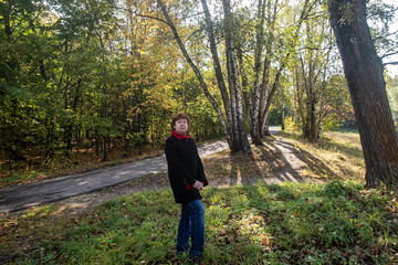Fototapeta premium Autumn. Lady in a black coat with a red collar on the background of bushes and trees in the park Kuskovo. Moscow