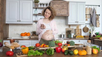 Young Pregnant Woman Looking For Recipe On Smartphone And Making Salad On Kitchen.