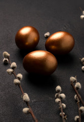Easter eggs on a black background next to willow branches close-up. Vertical image