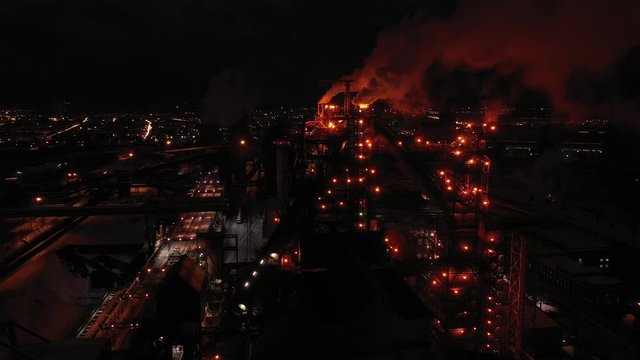 Top view of metallurgical plant blast furnace at night with smokestacks and fire blazing out of the pipe. Industrial panoramic landmark with blast furnance of metallurgical productio