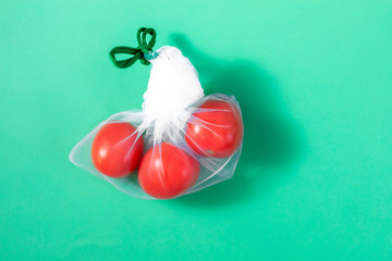 The reusable organza net bag for shopping with tomatoes is on the green background. Concept of no plastic, zero waste, reusable life. Flat lay. Copy space.