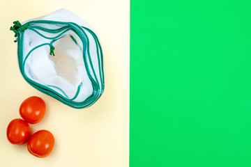 The reusable organza net bags for shopping with tomatoes are on green yellow background. Concept of...