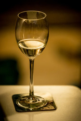 Isolated almost empty glass of white wine on a coaster with warm colors blurry background 