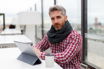 Young man sitting on a terrace in front of an electronic tablet and a reusable glass facing the camera