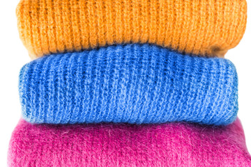 Pile of cozy winter woolen sweaters isolated on white. Vibrant colors, woman's fashion. Color match with classic blue tone clothes