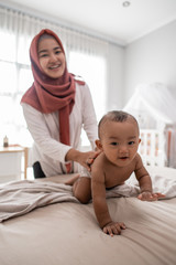 muslim mother giving a baby boy massage during diaper change