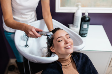 Professional hairdresser washing hair of a beautiful young adult woman in hair salon.