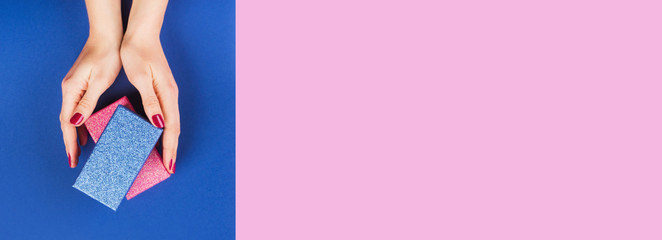 Elegant gift boxes stack in female hands with red manicure on pink and classic blue 2020 color...