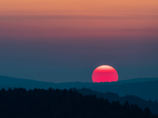 Sunset in the mountains with full disk of sunset under the horizon. Magical sunset in the Carpathians, orange sky, full disk of sunset. 