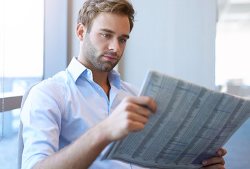 Young businessman reading the stock market report in newspaper