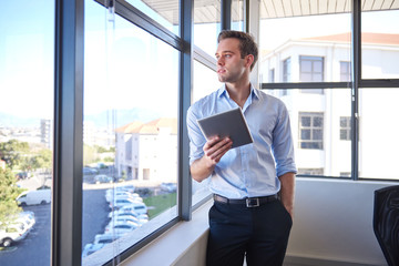Fototapeta premium Young businessman looking out window while holding digital tablet