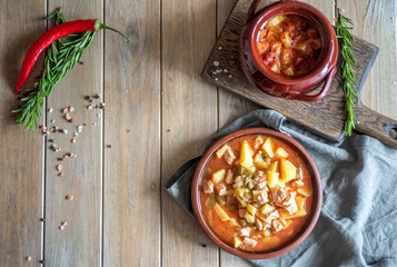 Meat with potatoes and vegetables stewed in a pot, clay plate with meat and potatoes on a gray background
