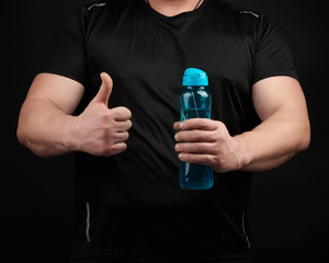 adult male athlete with muscles holds a plastic water bottle, with his right hand he shows a gesture like