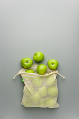 Green apples in a reusable cotton bag on a gray background.
