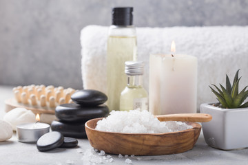 Fototapeta na wymiar Beauty still life of massage oil bottle of aroma essential and natural fragrance salt with stones, candles on concrete grey table. Composition of spa treatment