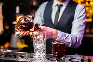 Close-up of expert bartender making cocktail in bar, splash of whiskey and rum.