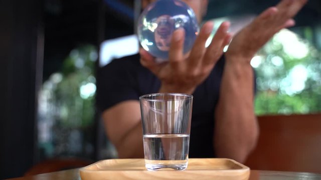 illusionist boy doing magic with a crystal ball and a glass of water in front of the static camera. Video in 4k