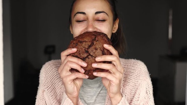 portrait of happy smiling woman eating big chocolate cookie and quite looking at the camera