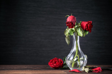 Withered rose on dark gray background and wooden table with fall petals and leaves, design concept...