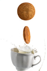 two cookies fall in a mug with milk and a splash on a white background