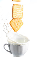 two cookies fall in a mug with milk and a splash on a white background