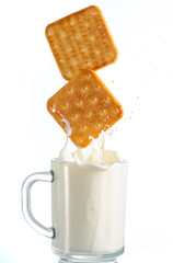 two cookies fall in a mug with milk and a splash on a white background