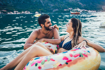 Happy woman in bikini floating on inflatable ring and her boyfriend in sea.