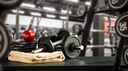 Black desk of free space for your decoration and blurred gym interior.Metal dumbbells and fit life 