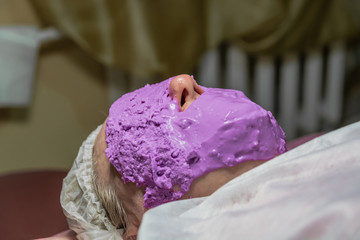 Cosmetic procedure with laying alginate masks on the face in a beauty salon. It is performed for an age woman. Improving skin turgor, rejuvenation and healing.