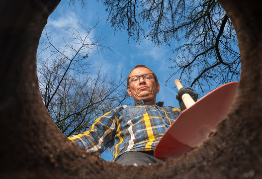 man with a shovel stands at a hole in the ground