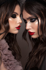 Art photo of two attractive girls with graphic cat eye makeup and red lips. One model is facing to another. Twins.