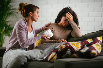 Woman broke up with boyfriend, she is crying and sister is trying to calm her down. Beautiful women sitting in living room.
