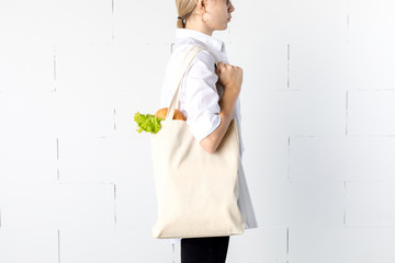 Girl is holding cotton eco-bag with green fresh kale and bread.