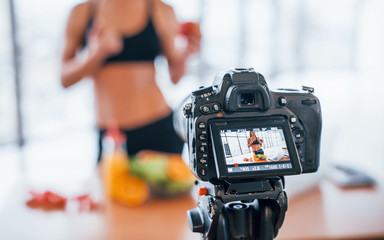 Female vlogger with sportive body standing indoors near table with healthy food
