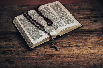 Top view Open Holy Bible and beads crucifix on a old oak wooden table. Beautiful red wall background.