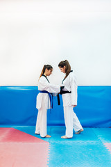 Two young women dress each other in their taekwondo suit