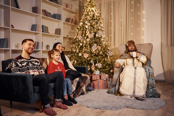 Happy family with guy in saint clothes celebrating new year in christmas decorated room