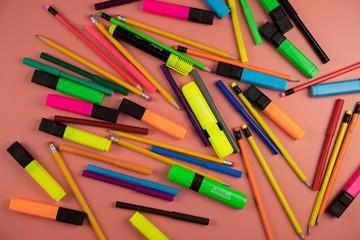 many multi-colored pencils and markers on a pink background, close-up top view,funny background